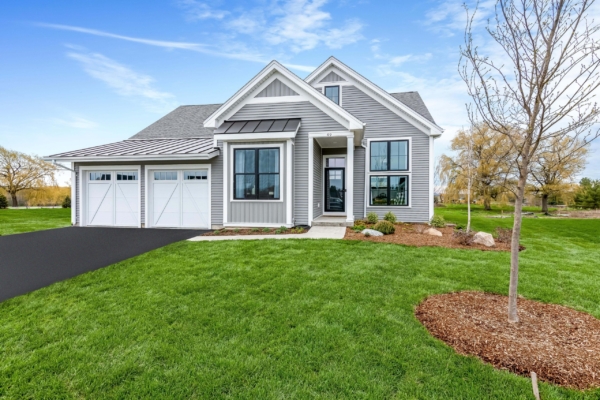 New modern suburban house with a large green lawn, driveway, and well-maintained landscaping, under a clear blue sky.