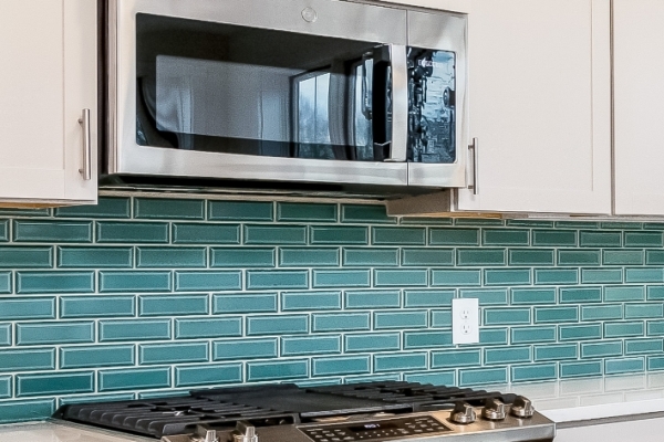 Modern kitchen with stainless steel microwave above a gas stove and teal subway tile backsplash. white cabinets add a clean look.