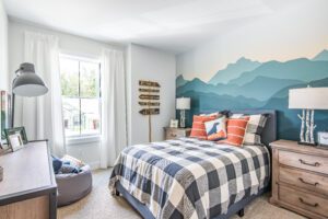 Modern bedroom with a mountain mural on the wall, plaid bedding, wooden furniture, and a large window.