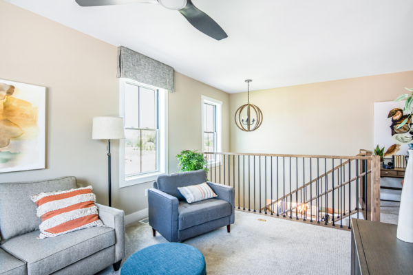 Brightly lit modern living room with a gray sofa, blue armchair, circular chandelier, and large windows.