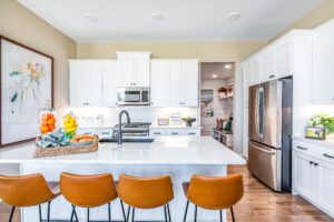 Modern kitchen interior with white cabinetry, stainless steel appliances, a central island with brown leather stools, and decorative elements.