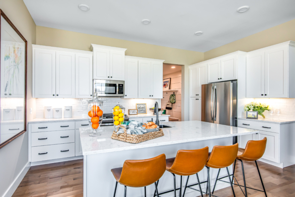 Modern kitchen with white cabinetry, stainless steel appliances, and a central island with orange bar stools.