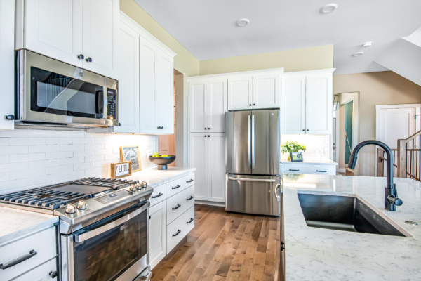 Modern kitchen interior with white cabinetry, stainless steel appliances, marble countertops, and a subway tile backsplash.