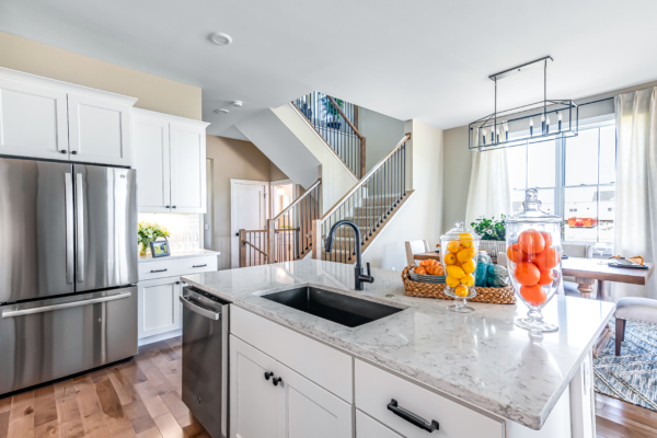 Modern kitchen featuring white cabinets, marble countertops, stainless steel appliances, and a view of the staircase and living area.
