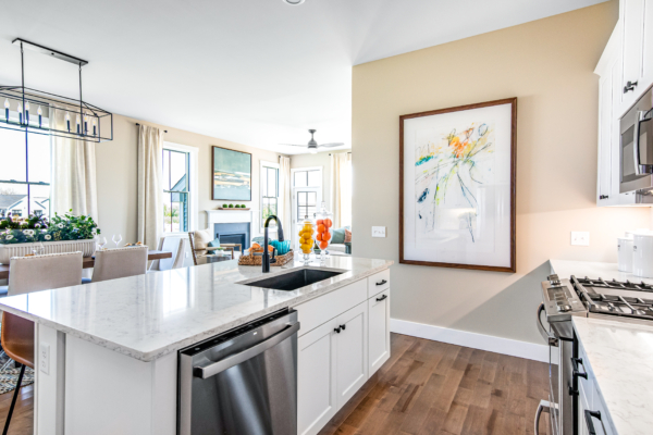 Modern kitchen with white cabinets, marble countertops, stainless steel appliances, and an adjoining living area with natural light.