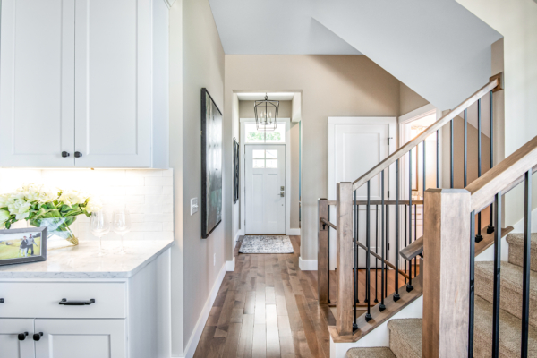 Bright, modern home interior featuring a white kitchen on the left, a hallway with a staircase on the right, and a hanging lantern light fixture.