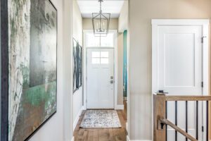Modern home entrance with a white door, hallway featuring a large abstract painting on the wall, and a pendant light hanging above.