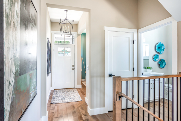 Brightly lit home interior featuring a foyer with hardwood floors, a white door, abstract wall art, and a modern hanging light fixture.