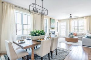 Bright, modern dining and living room with large windows, wooden flooring, a dining table set for six, and a cozy sitting area with a round coffee table.