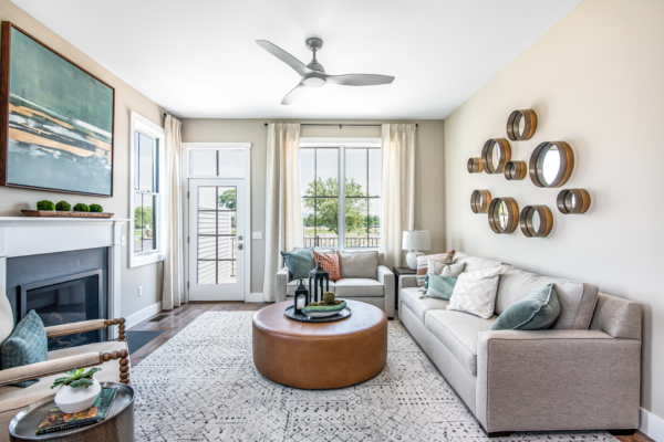 Bright living room with a sectional sofa, round wooden coffee table, fireplace, and wall decor, opening onto a balcony with french doors.