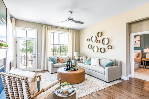 Modern living room with beige walls, large windows, and stylish decor including a grey sofa, leather ottoman, and round wall mirrors.