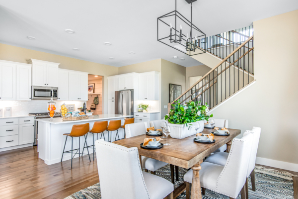 Bright, modern kitchen with white cabinets and a central island with orange stools, connected to a dining area with a wooden table set for a meal.