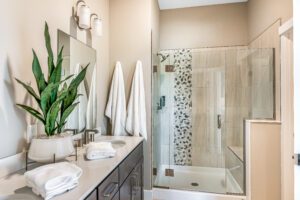 Modern bathroom interior with a double vanity sink, large mirrors, a glass-enclosed shower, and a potted plant.