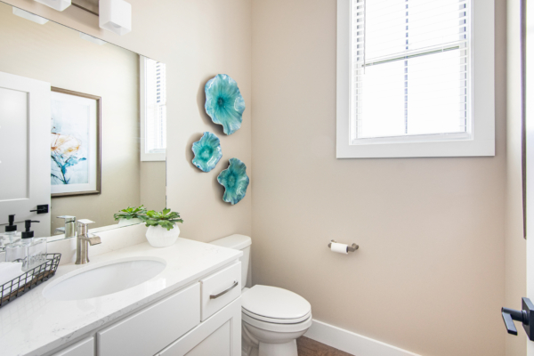 Bright bathroom with a white vanity topped with a marble counter, a large mirror, decorative blue wall flowers, and a small potted plant.
