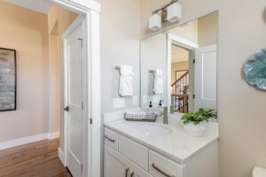 A modern bathroom with a white vanity, marble countertop, and large mirror reflecting a staircase and artwork on adjacent walls.