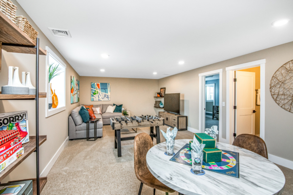 A modern, bright game room featuring a foosball table, a round dining table with chairs, and a cozy sitting area with a sofa and vibrant wall art.