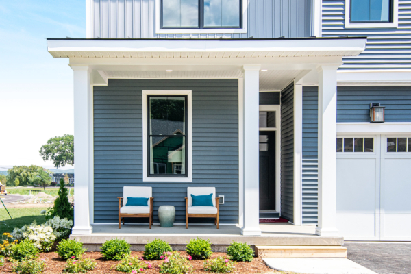 Modern two-story house with gray siding, white trim, a covered front porch with two chairs, and a landscaped front yard.