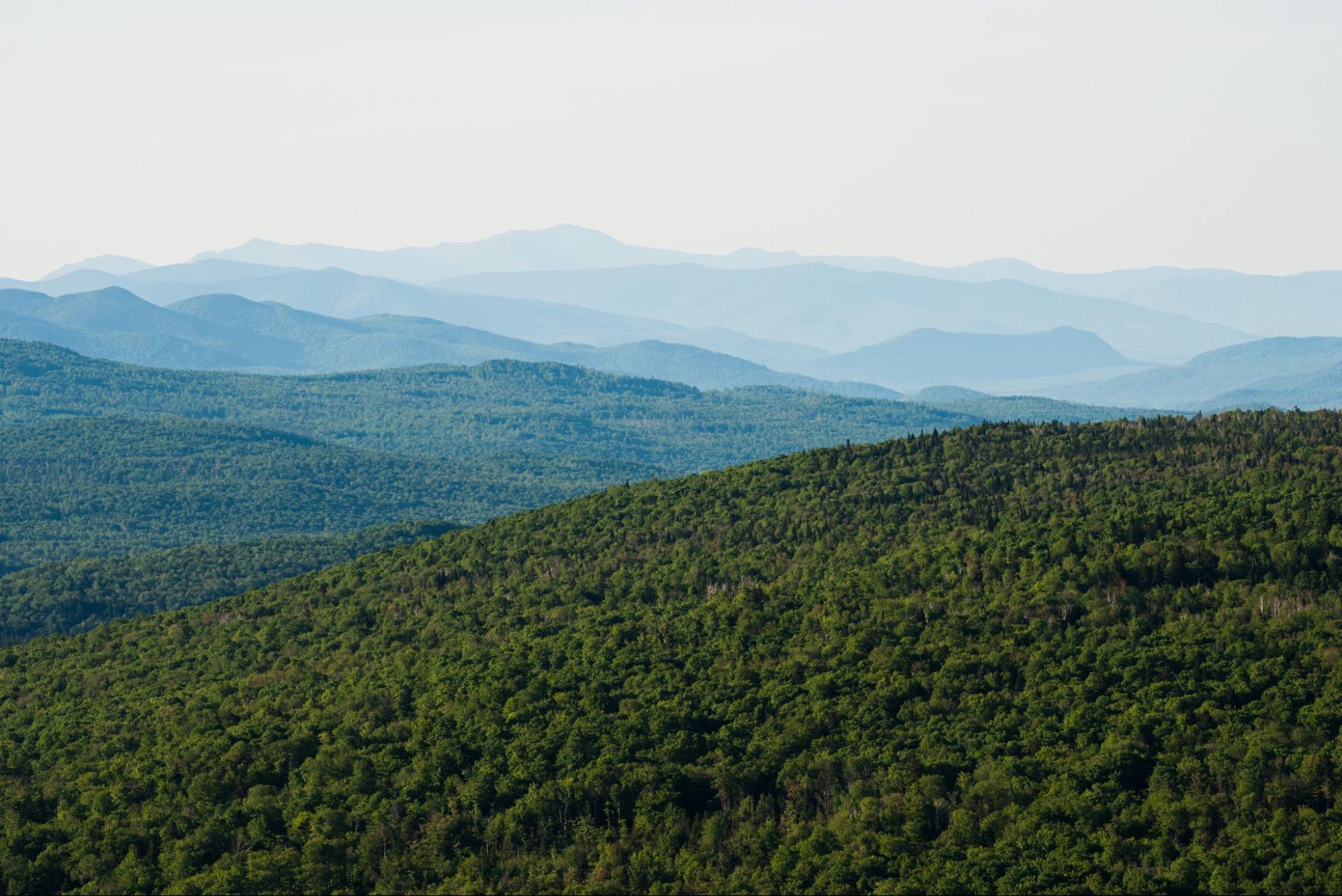 Green forested hills and blue mountains offer classic Vermont activities under a clear sky.
