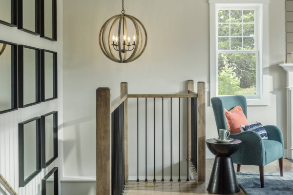 An elegant home interior featuring a staircase with black railings, a blue chair beside a round side table, and a spherical chandelier above.