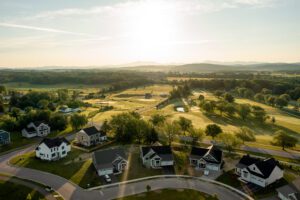 Aerial view of a suburban neighborhood with houses, roads, and a golf course, set against a backdrop of mountains and a sunrise.