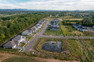 Aerial view of Spear Meadows suburban houses, a small pond, and greenery under a partly cloudy sky.