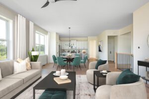 Modern open-plan living space with a beige sofa, round coffee table, and teal dining chairs set against white interiors and ample natural light.