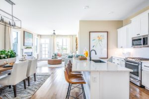 Bright, open-plan kitchen and living area with modern furnishings, large windows, and a kitchen island with bar stools.