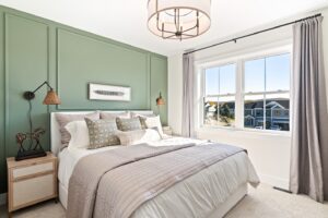 Bright bedroom with green accent wall, large bed, neutral bedding, and sunlight streaming through window.