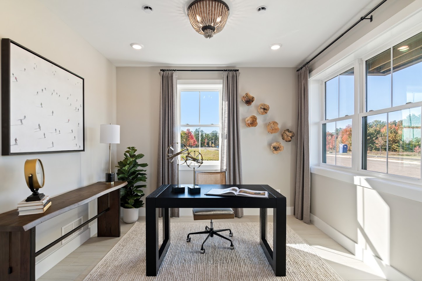 Modern home office with a black desk, art on the wall, large windows, and natural light streaming in.