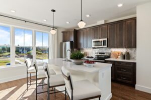 Modern kitchen with dark wood cabinets, white island, pendant lights, and large window with outdoor view.