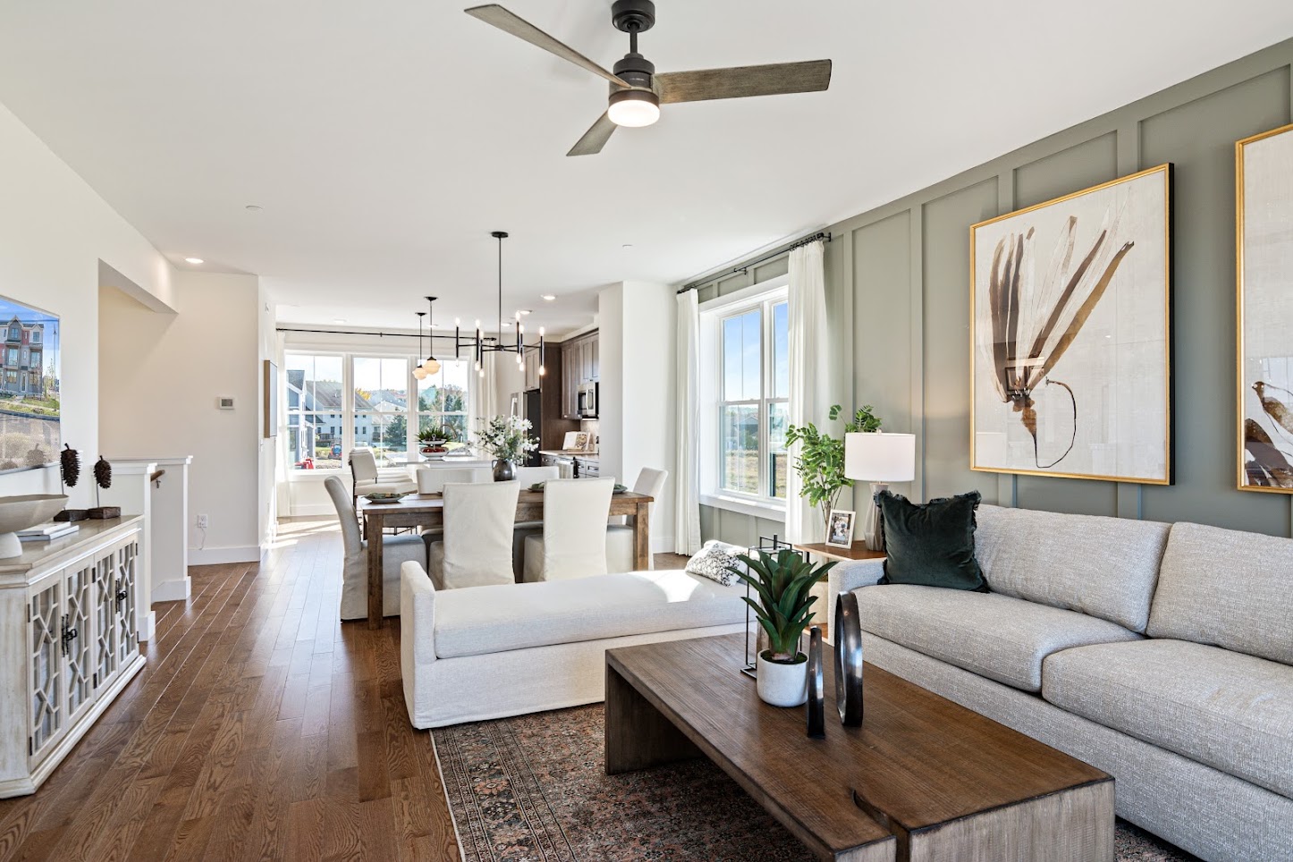 Modern living and dining room with light furniture, wood floors, large windows, and framed artwork on the wall.