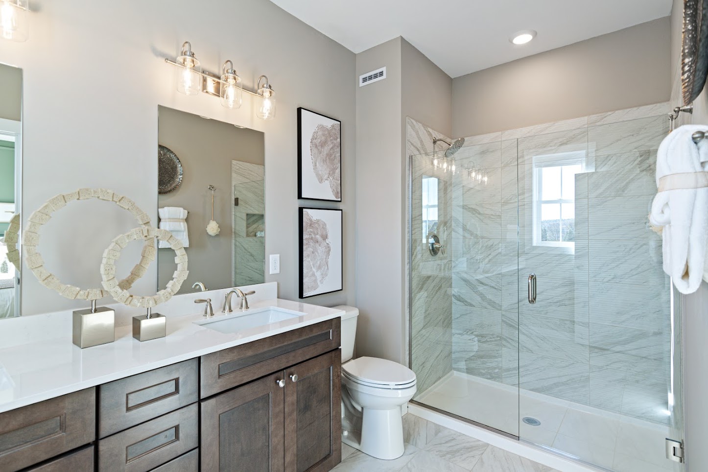 Modern bathroom with double sink, large mirror, glass shower, and neutral decor with marble accents.
