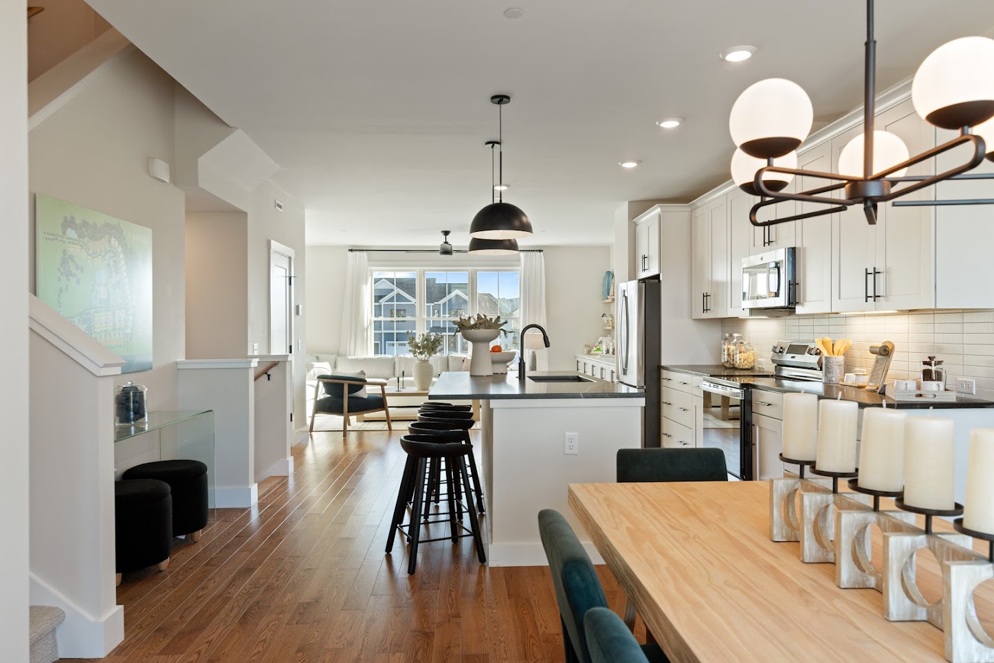 Modern open-plan kitchen and dining area with wood floors, white cabinets, and stylish lighting fixtures.