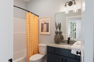 Modern bathroom with a yellow checkered shower curtain, dark vanity, and decorative art above the toilet.