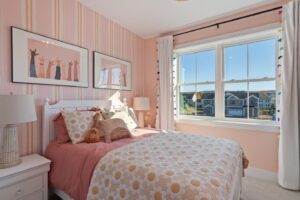 Bright pink bedroom with a sun-patterned bed, two lamps, playful wall art, and a large window with white curtains.