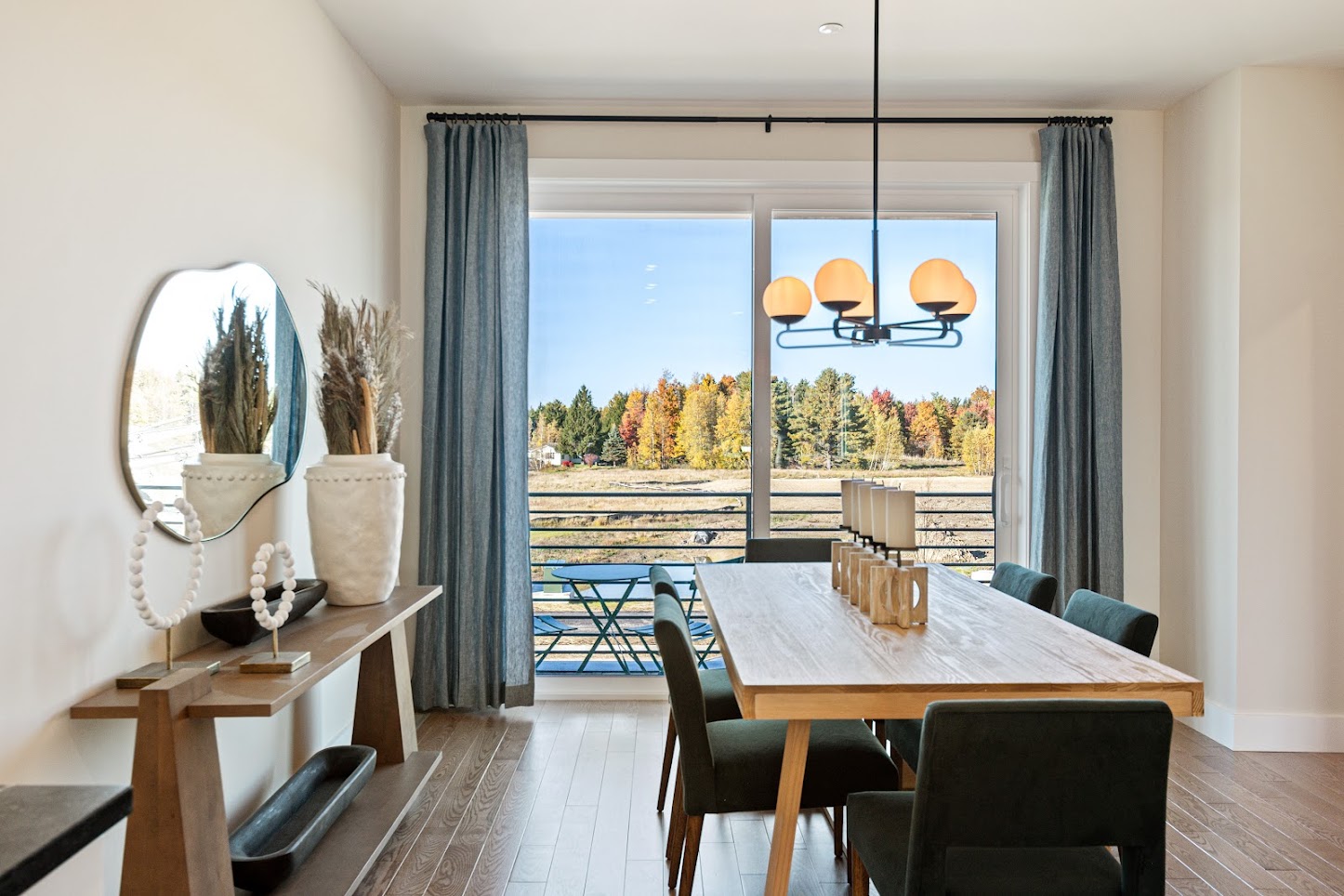 Modern dining room with wooden table, green chairs, large window, and autumn trees visible outside.