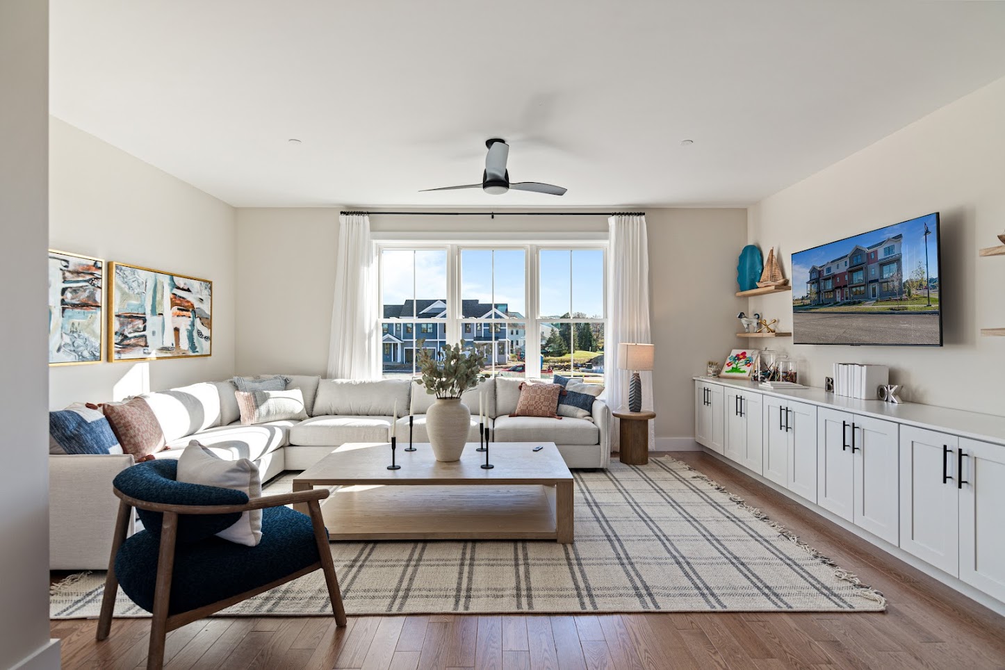 Bright living room with a large sectional sofa, armchair, TV, and large windows letting in natural light.