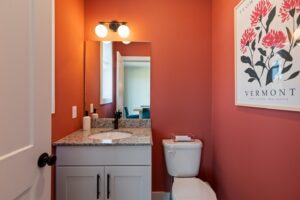 Small bathroom with red walls, granite countertop, white vanity, and a Vermont flower poster above the toilet.