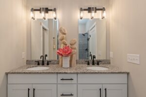 Bathroom vanity with double sinks, granite countertop, modern lights, and pink flower arrangement between mirrors.