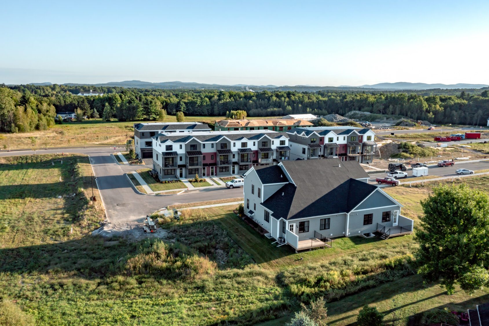 Aerial view of new townhouses and a single-family home in a suburban neighborhood surrounded by greenery.
