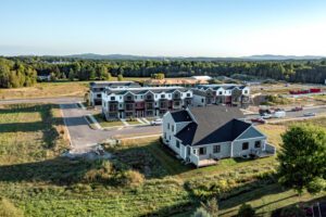 Aerial view of new townhouses and a single-family home in a suburban neighborhood surrounded by greenery.