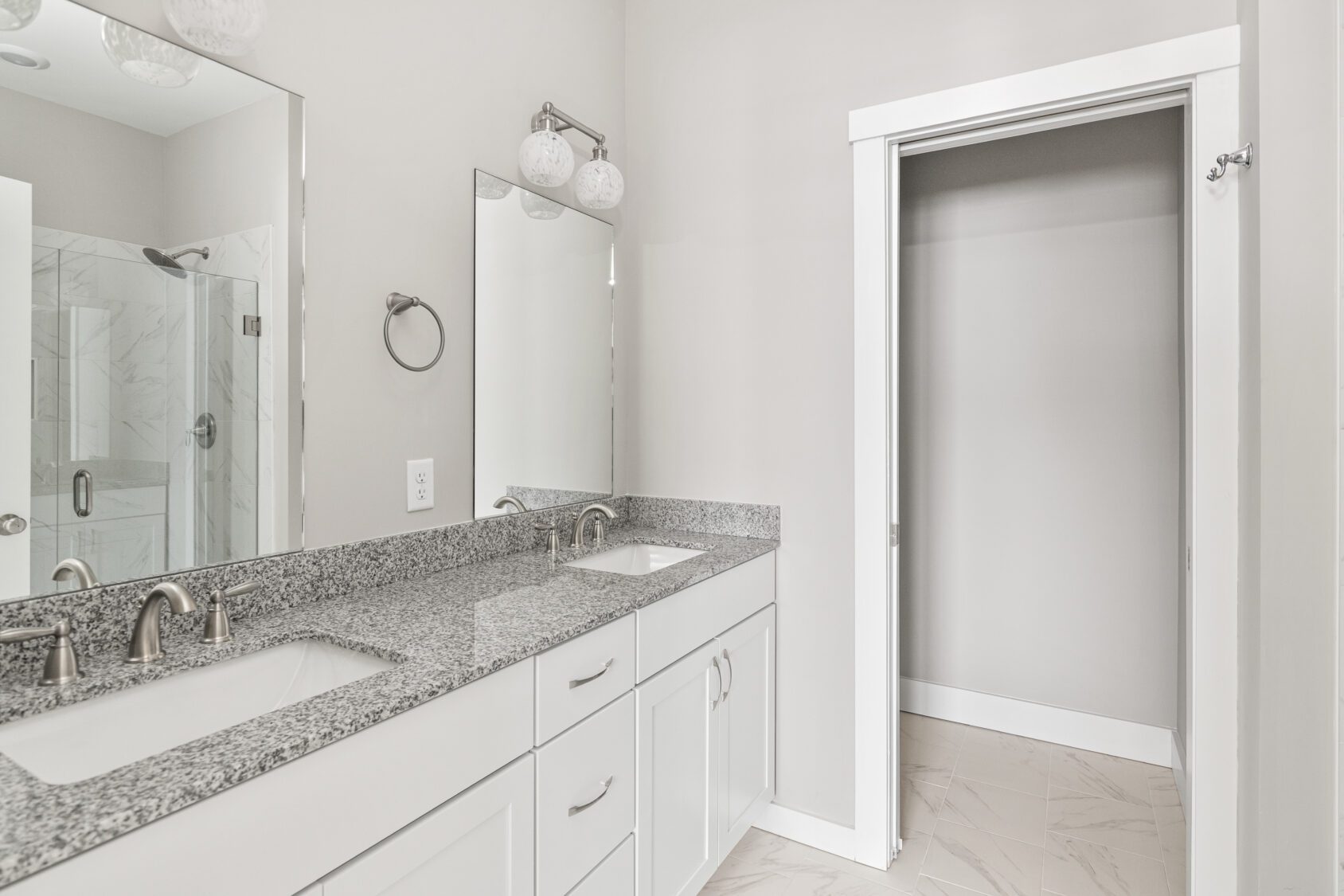 Modern bathroom with double sinks, granite countertop, mirrors, and an open empty closet with sliding door.