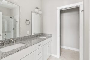 Modern bathroom with double sinks, granite countertop, mirrors, and an open empty closet with sliding door.