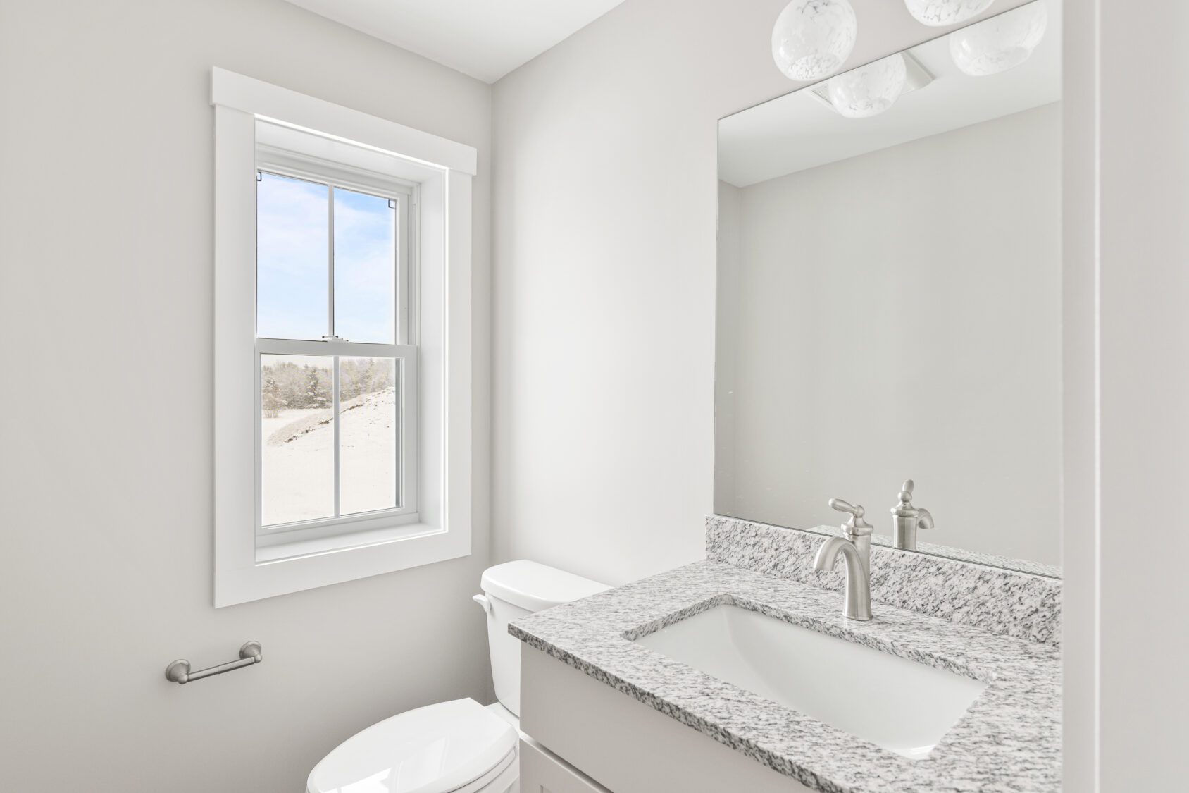 Bright, modern bathroom with a granite countertop, large mirror, and a window letting in natural light.