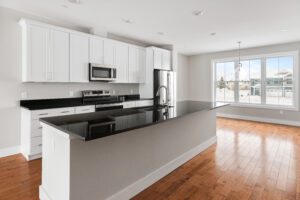 Modern kitchen with white cabinets, black countertops, stainless steel appliances, and large windows.