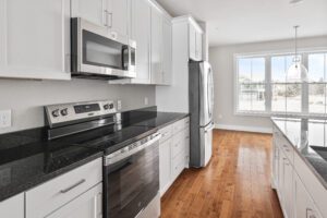 Modern kitchen with white cabinets, stainless steel appliances, black countertops, and wood flooring.