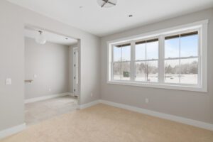Bright, empty room with beige carpet, large window, and view of a snowy landscape outside.