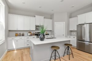 Modern kitchen at 71 Elm Street with white cabinets, a large island, two stools, and a stainless steel refrigerator.