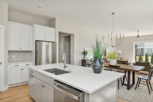Modern kitchen at 71 Elm Street with white cabinets, a center island sink, and open dining and living areas in back.