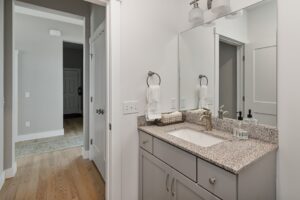 Modern bathroom at 71 Elm Street with gray cabinets, granite countertop, mirror, and towel ring by the hallway.